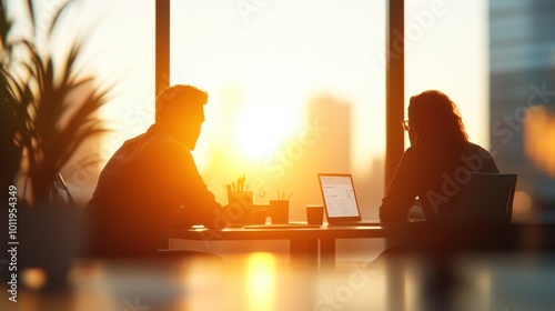 A pair of colleagues engaged in a focused discussion at a table, illuminated by the soft light of sunrise, symbolizing new beginnings and innovation. photo