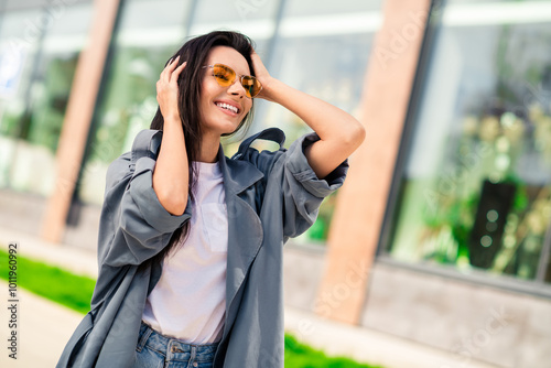 Photo of cheerful pretty lady dressed grey jacket dark eyewear smiling walking enjoying sunshine outdoors town street