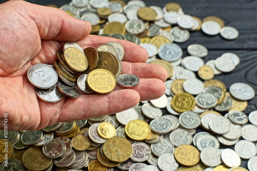 many Ukrainian iron white and yellow with symbols of banking national different financial shiny round coins in the hand of a poor man against the background of a black table and change photo