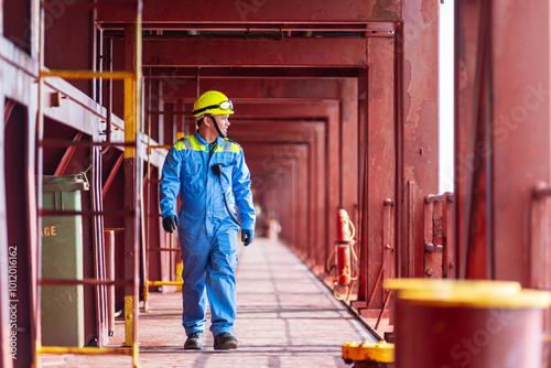 A deck officer of a merchant ship walking across the deck towards the maneuvering station during docking operations at the port, focused and ready for the task ahead.