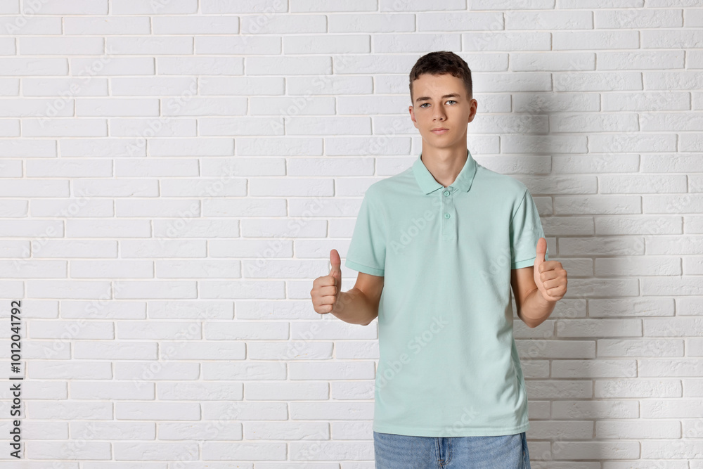 Teenage boy wearing light green t-shirt and showing thumbs up near white brick wall, space for text Teenage boy wearing light green t-shirt and showing thumbs up near white brick wall, space for text