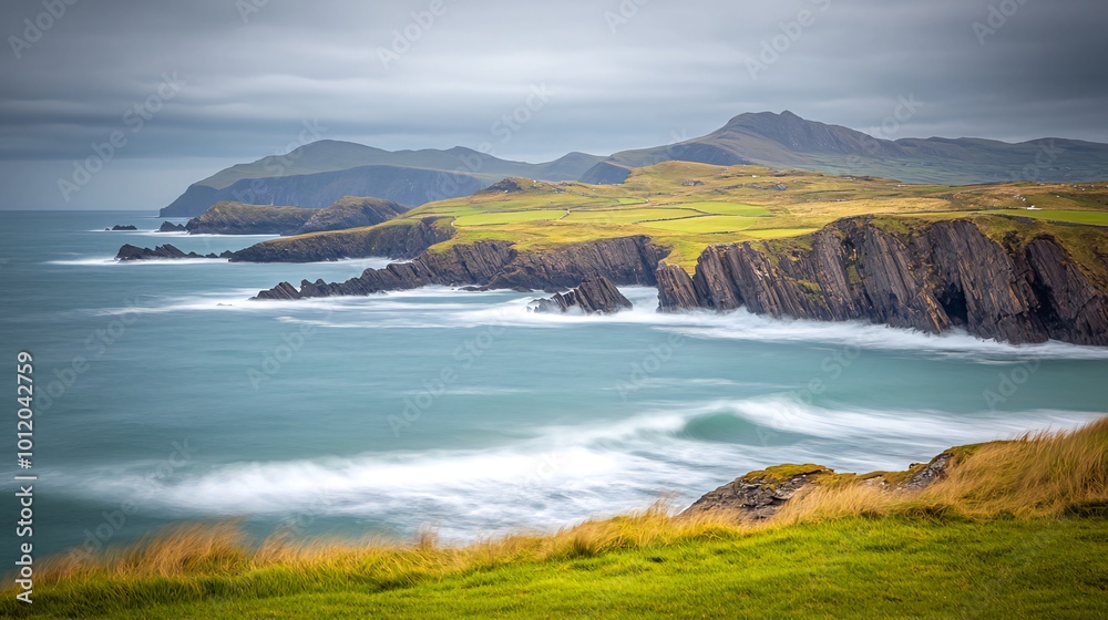 Dramatic, sweeping view of a rugged coastline with crashing waves, green hills, and a cloudy sky. Dramatic, sweeping view of a rugged coastline with crashing waves, green hills, and a cloudy sky.