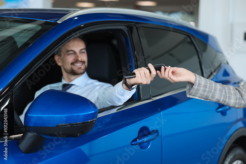 Saleswoman giving key to client inside new car in salon, selective focus