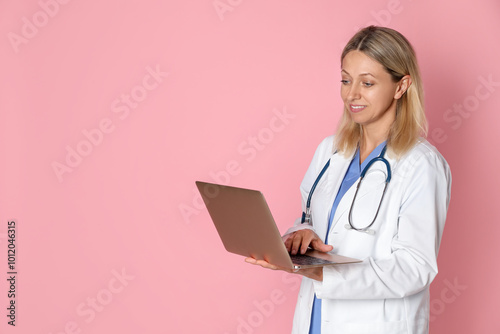 Doctor in medical uniform with stethoscope and laptop on pink background, space for text