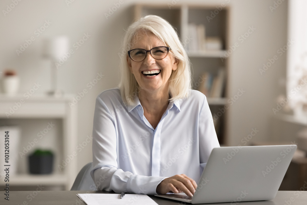 Portrait of happy middle-aged businesslady working on laptop sit at desk in office, look at camera, chatting, lead correspondence, respond to client, enjoy professional achievements and productivity Portrait of happy middle-aged businesslady working on laptop sit at desk in office, look at camera, chatting, lead correspondence, respond to client, enjoy professional achievements and productivity