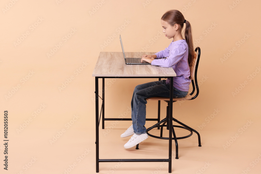 Girl with correct posture using laptop at wooden desk on beige background Girl with correct posture using laptop at wooden desk on beige background