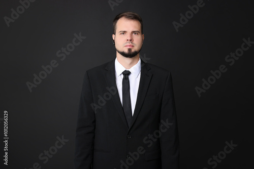 Young bodyguard in suit with earpiece on black background