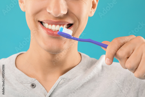 Young man brushing his teeth on light blue background, closeup