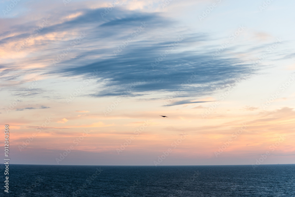 Pastel clouds drift across the sky, the colors blending softly into the horizon. The Atlantic Ocean below lies calm, reflecting the fading light as day gives way to night.