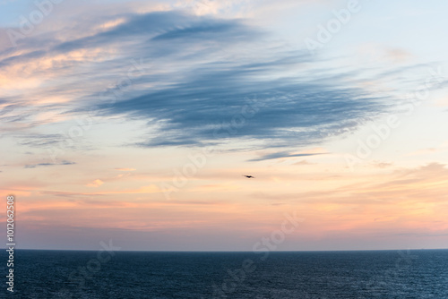 Pastel clouds drift across the sky, the colors blending softly into the horizon. The Atlantic Ocean below lies calm, reflecting the fading light as day gives way to night.