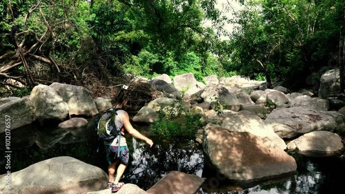 A tourist moves along large boulders in the bed of a mountain river