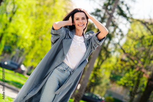 Portrait photo of beautiful young smiling latin attractive lady wearing gray coat walking outdoors relaxed posing stylish outfit in nature