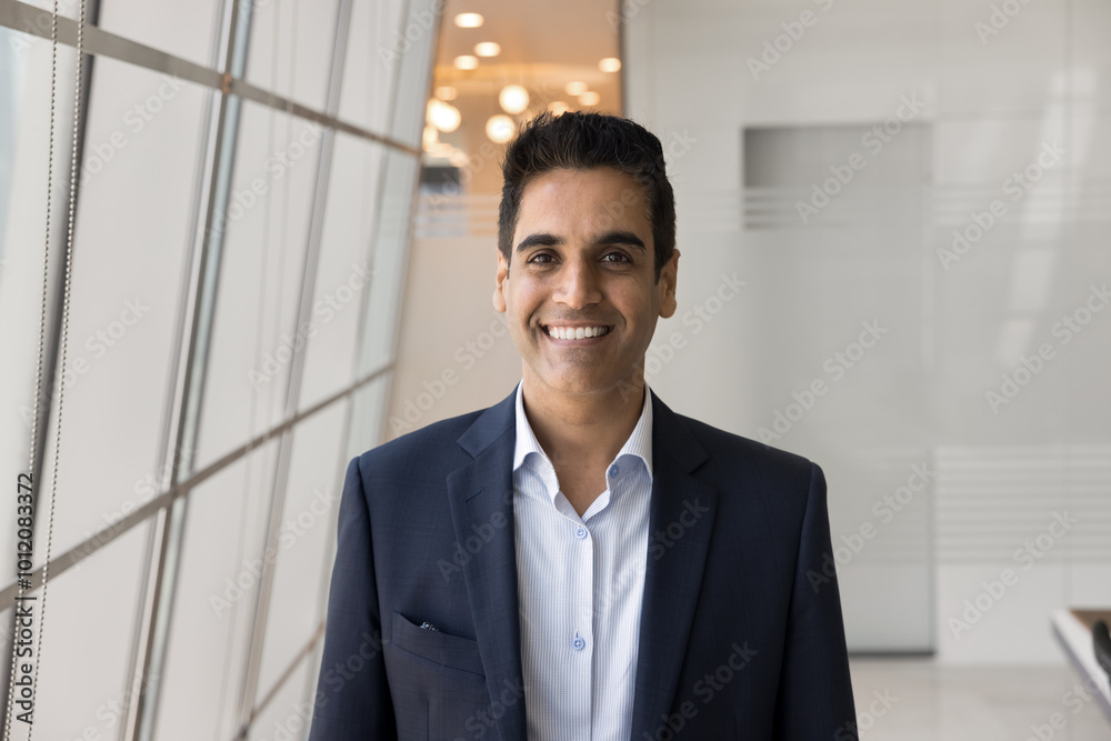 Happy handsome Indian business leader man in formal clothes posing in modern office space, looking at camera with toothy smile. Successful professional, executive, CEO head shot portrait Happy handsome Indian business leader man in formal clothes posing in modern office space, looking at camera with toothy smile. Successful professional, executive, CEO head shot portrait