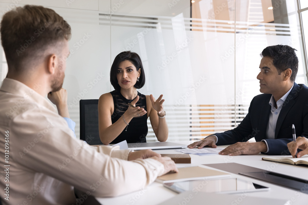 © fizkes - Serious confident young female boss woman holding meeting with diverse colleagues, talking to multiethnic team at large office table, discussing company leadership, project management