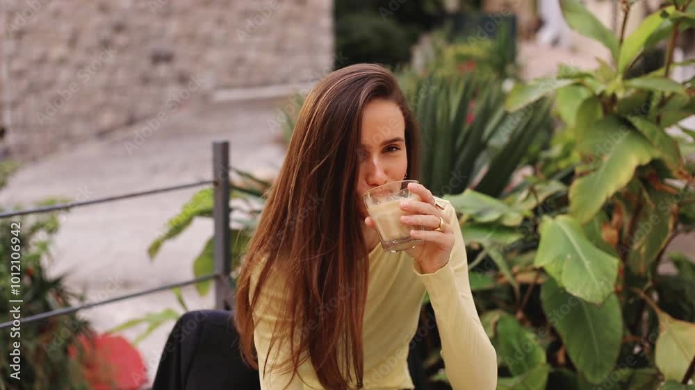Brunette long hair woman hold glass of water and glass of latte, take glass of latte, good choice sitting in outside cafe near green flowers. Woman choose coffee. Water or cappuccino. Decision. Brunette long hair woman hold glass of water and glass of latte, take glass of latte, good choice sitting in outside cafe near green flowers. Woman choose coffee. Water or cappuccino. Decision.