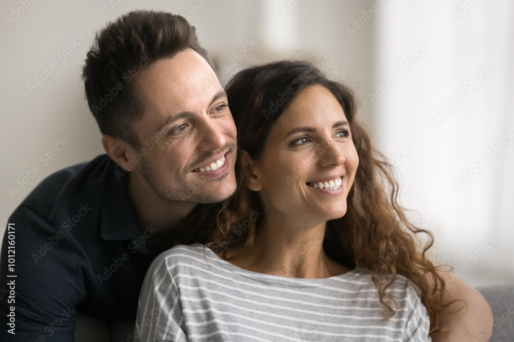 Happy dreamy couple in love sitting close with head touches, looking at window away with toothy smiles, discussing plans, house buying, mortgage, enjoying closeness, good relationship Happy dreamy couple in love sitting close with head touches, looking at window away with toothy smiles, discussing plans, house buying, mortgage, enjoying closeness, good relationship