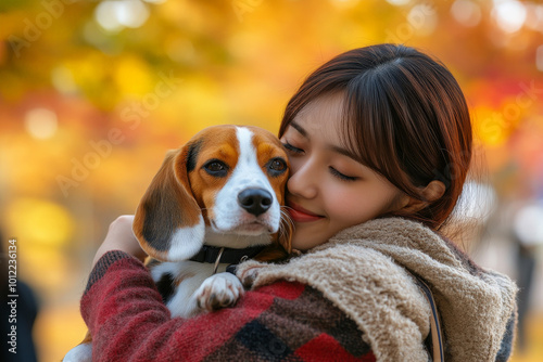 A young adult Japanese woman, hugging a cute beagle puppy in a bustling urban park filled with autumn leaves. The vibrant colors of the setting create a beautiful backdrop for their affectionate