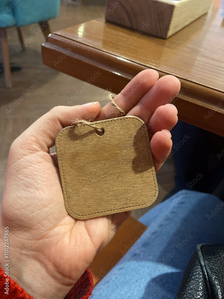 Obraz premium Close-up hand holds a small wooden tag with a twine loop. Copy space and empty place for text. Natural texture and simplicity of the tag create a connection to artisanal craftsmanship