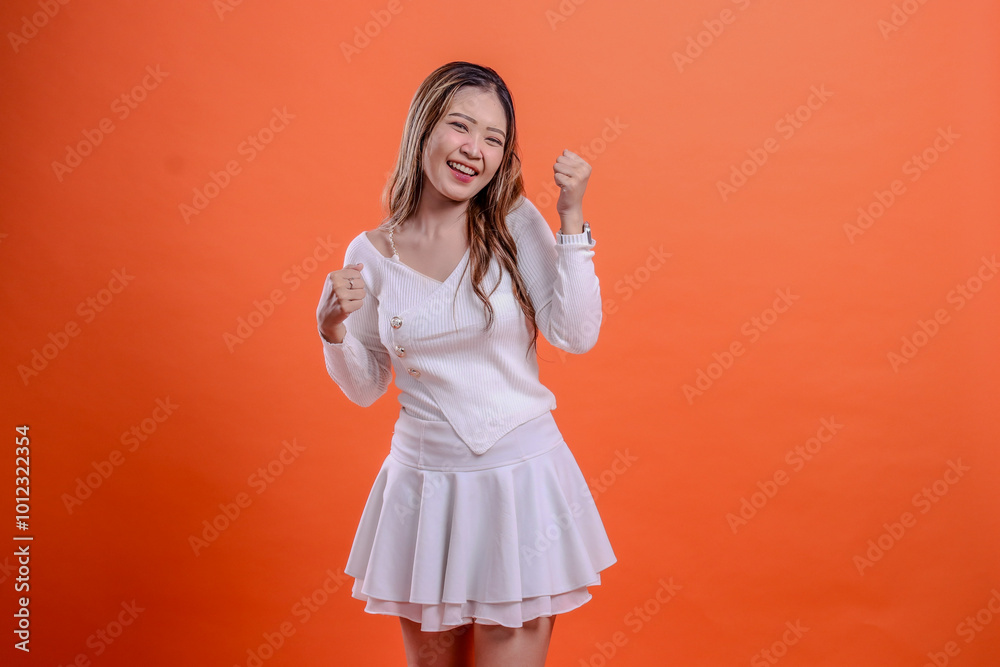 expression of beautiful young woman female in white top standing cheerful to camera both hands clenched successfully up down isolated orange background. for fashion concept, promotion, commercial expression of beautiful young woman female in white top standing cheerful to camera both hands clenched successfully up down isolated orange background. for fashion concept, promotion, commercial