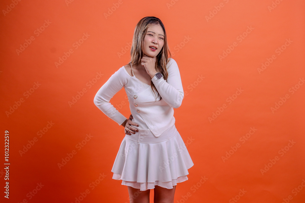 gesture young beautiful indonesia woman white top standing candid close eyes pain sore throat hands hold waist and neck isolation orange background. for health, advertising, science, commercial gesture young beautiful indonesia woman white top standing candid close eyes pain sore throat hands hold waist and neck isolation orange background. for health, advertising, science, commercial