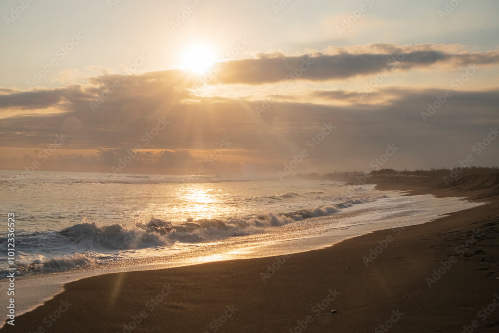 The evening view before sunset on the beach. The sky is orange and the sun is shining brightly. Beautiful black sand coastline The evening view before sunset on the beach. The sky is orange and the sun is shining brightly. Beautiful black sand coastline