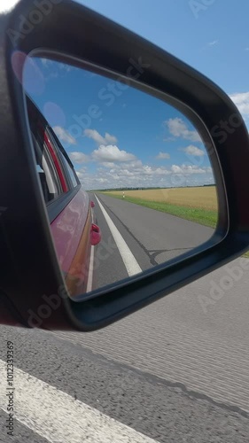 Video shooting in motion, view in the rear view side mirror of a auto, driving a red car along the road