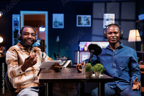 Two black men host a live talk show, discussing various topics while interacting with fans. They use professional microphones to create high-quality content for an online streaming service. photo