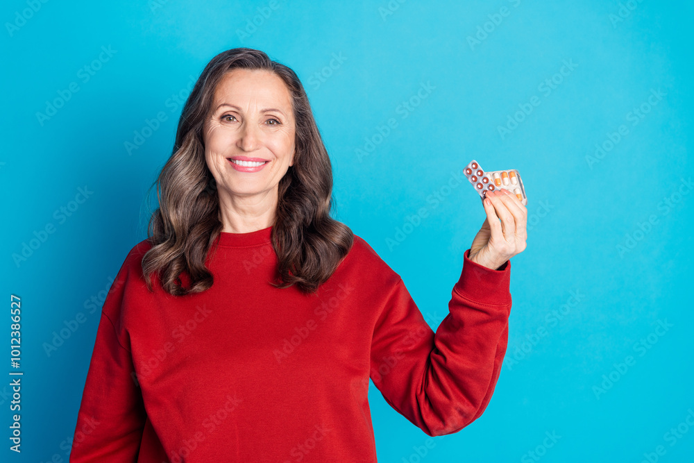 Obraz premium Portrait of nice aged woman hold pills wear red sweater isolated on blue color background