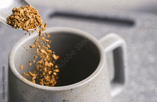 Grains of freeze dried instant coffee,falling from a silver tea spoon,into an empty cup,on a slate grey background..