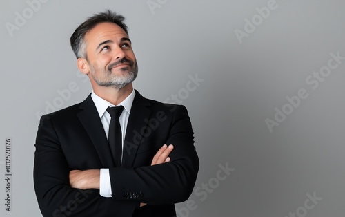 A confident man in a suit stands with arms crossed, looking upward, conveying a sense of optimism and contemplation against a neutral background.