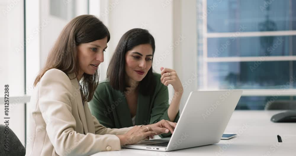 Two businesswomen using laptop in boardroom discuss business-related matters. Analyze sales performance and strategies to boost revenue, review market research data, planning upcoming business project Two businesswomen using laptop in boardroom discuss business-related matters. Analyze sales performance and strategies to boost revenue, review market research data, planning upcoming business project