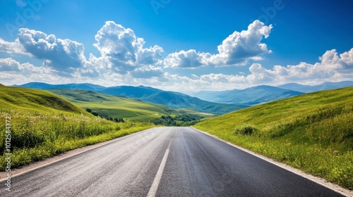 A scenic asphalt road through green hills and mountains, with a clear sky and puffy white clouds on a sunny day.