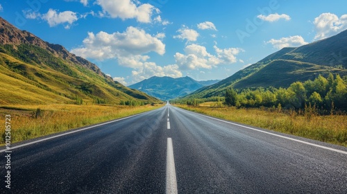 A scenic asphalt road with green mountains and blue sky, under the warm sunlight of a clear, cloud-speckled afternoon.