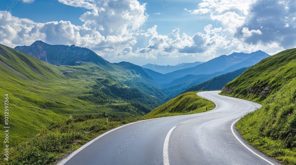 Fototapeta premium A winding asphalt road with green mountains on either side, under a bright sky and scattered clouds on a sunny afternoon.