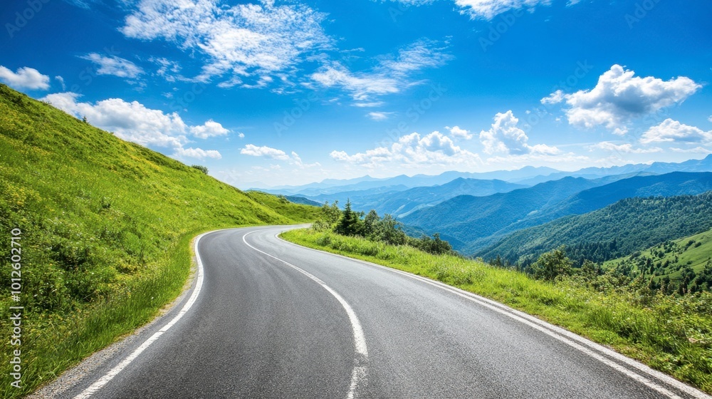 Naklejka premium An asphalt road winding through green mountain valleys, with a clear blue sky and scattered clouds on a sunny day.