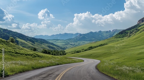 An asphalt road winding through green mountain valleys, with a clear sky and soft white clouds on a sunny, bright day.