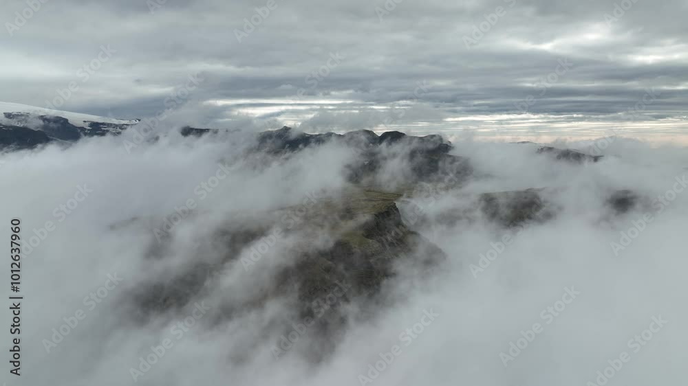 A dramatic aerial shot of fog rolling over mountain peaks in Hafursey, Iceland, with a moody sky and distant glaciers. A dramatic aerial shot of fog rolling over mountain peaks in Hafursey, Iceland, with a moody sky and distant glaciers.