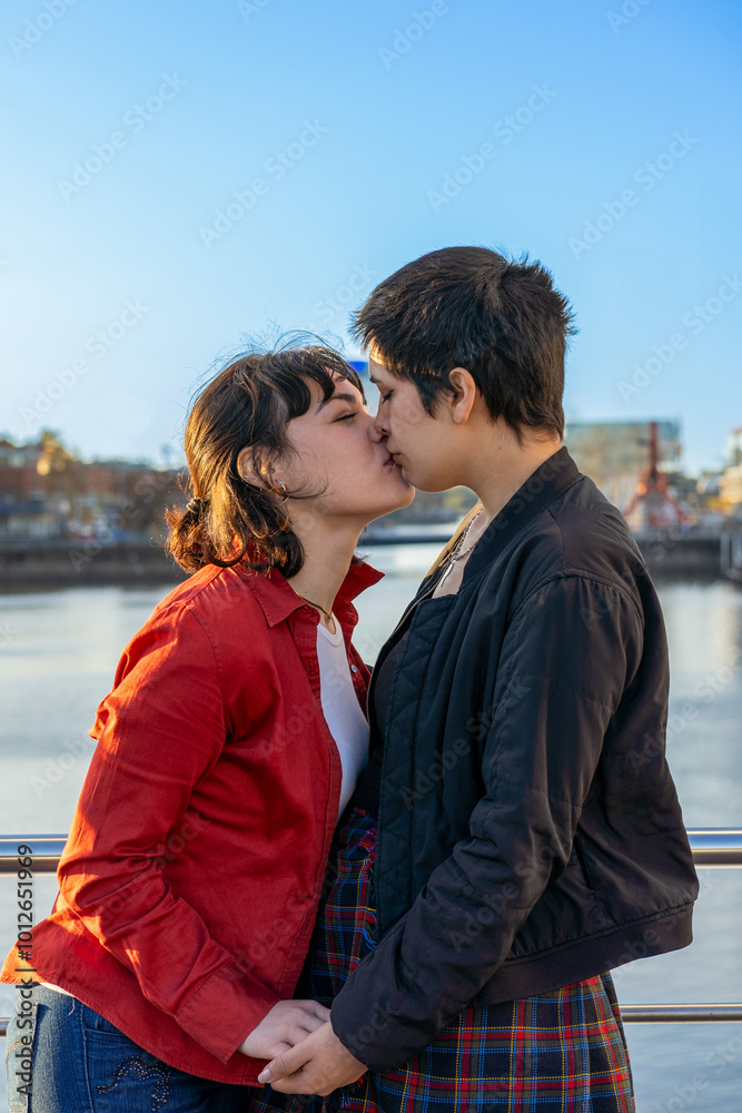 Fototapeta premium Young lesbian couple lovingly entwined, sharing a kiss while holding hands