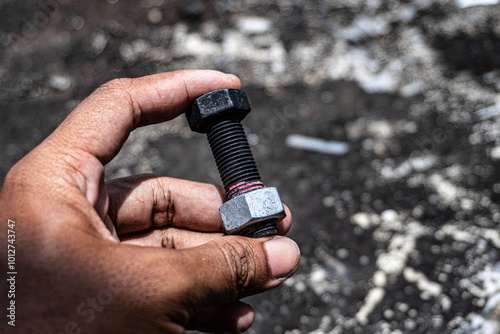 close-up photograph of a human hand firmly gripping a black hex bolt with a silver nut.