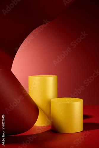 A minimalist product display features golden cylinder podiums against vibrant red paper, creating a dynamic and eye-catching composition with a curved and flowing form.