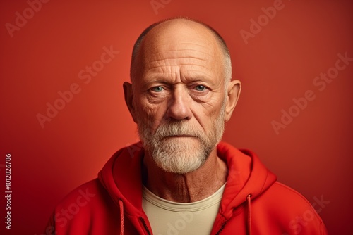 Portrait of a senior man in a red hoodie on a red background.