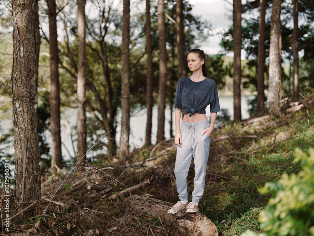 Thoughtful young woman standing on a log in a forest, wearing comfortable casual attire, enjoying nature and reflecting amidst serene surroundings Thoughtful young woman standing on a log in a forest, wearing comfortable casual attire, enjoying nature and reflecting amidst serene surroundings
