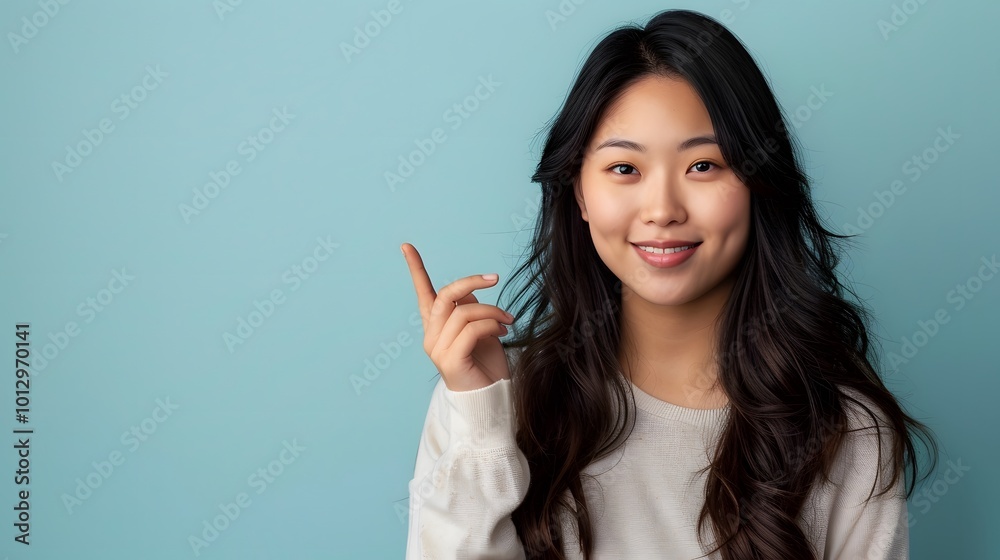 Asian woman presenting and pointing with copy space against a light blue background, showcasing beauty, confidence, and elegance Asian woman presenting and pointing with copy space against a light blue background, showcasing beauty, confidence, and elegance