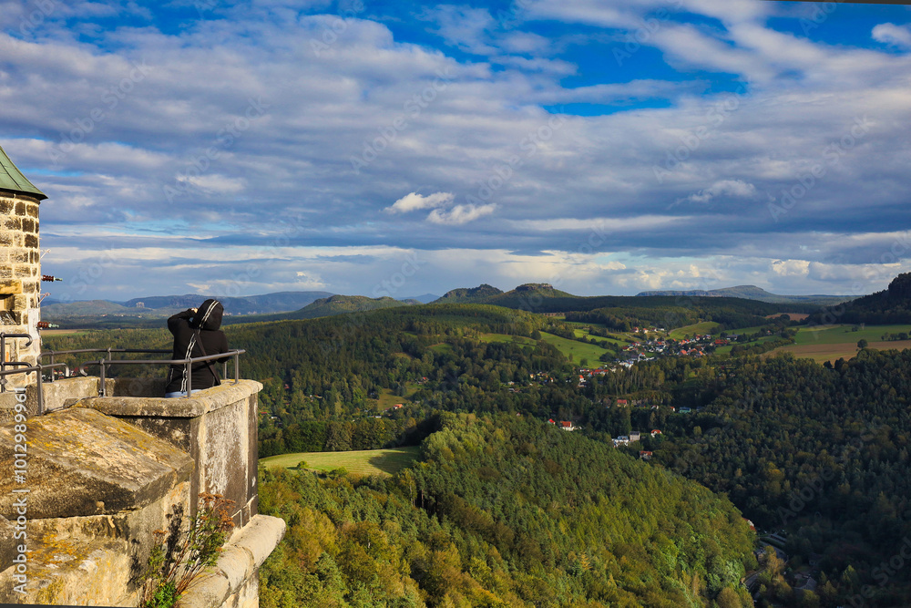 Fototapeta premium Ein Fotograf blickt von einer steinernen Bastion der Festung Königstein über die herbstliche Hügellandschaft und die Tafelberge der Sächsischen Schweiz, Königstein, Sachsen, Deutschland