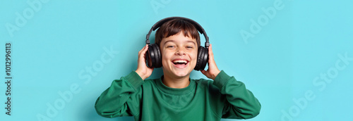 Happy smiling boy in black headphones and green sweatshirt on bright blue background