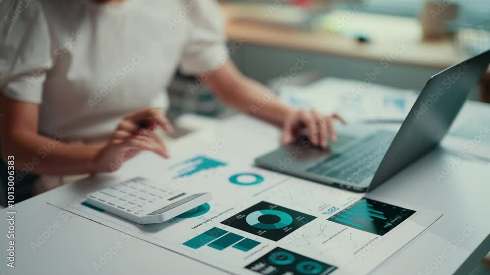 Businesswoman working on financial data while using a calculator and laptop. Analyzing charts and graphs, she focuses on accounting and strategic planning in a corporate environment