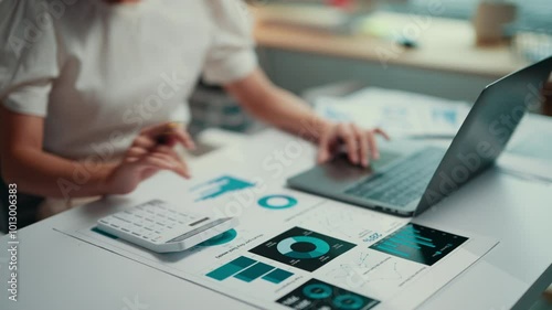 Businesswoman working on financial data while using a calculator and laptop. Analyzing charts and graphs, she focuses on accounting and strategic planning in a corporate environment