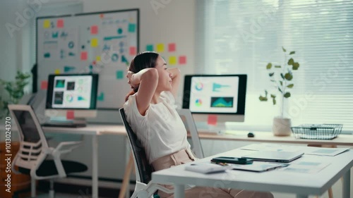 Young businesswoman working on a laptop in a modern office takes a break to stretch, promoting well-being and productivity in a dynamic work environment