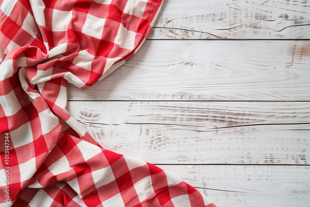 Naklejka premium A red and white checkered tablecloth lies on a wooden background.