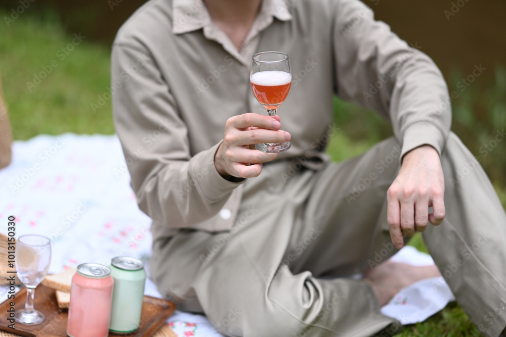 Close up image of A person holds a glass of sparkling drink, enjoying a peaceful moment during a picnic Close up image of A person holds a glass of sparkling drink, enjoying a peaceful moment during a picnic